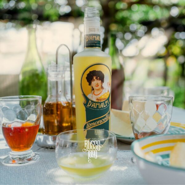 Bottiglia di Limoncello d’Amalfi IGP in primo piano, con scorci della Costiera Amalfitana sullo sfondo